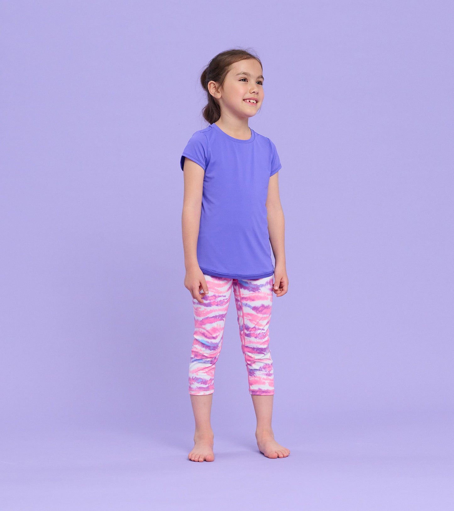 Purple short-sleeve t-shirt with a smooth finish, worn by a girl paired with colorful patterned leggings.
