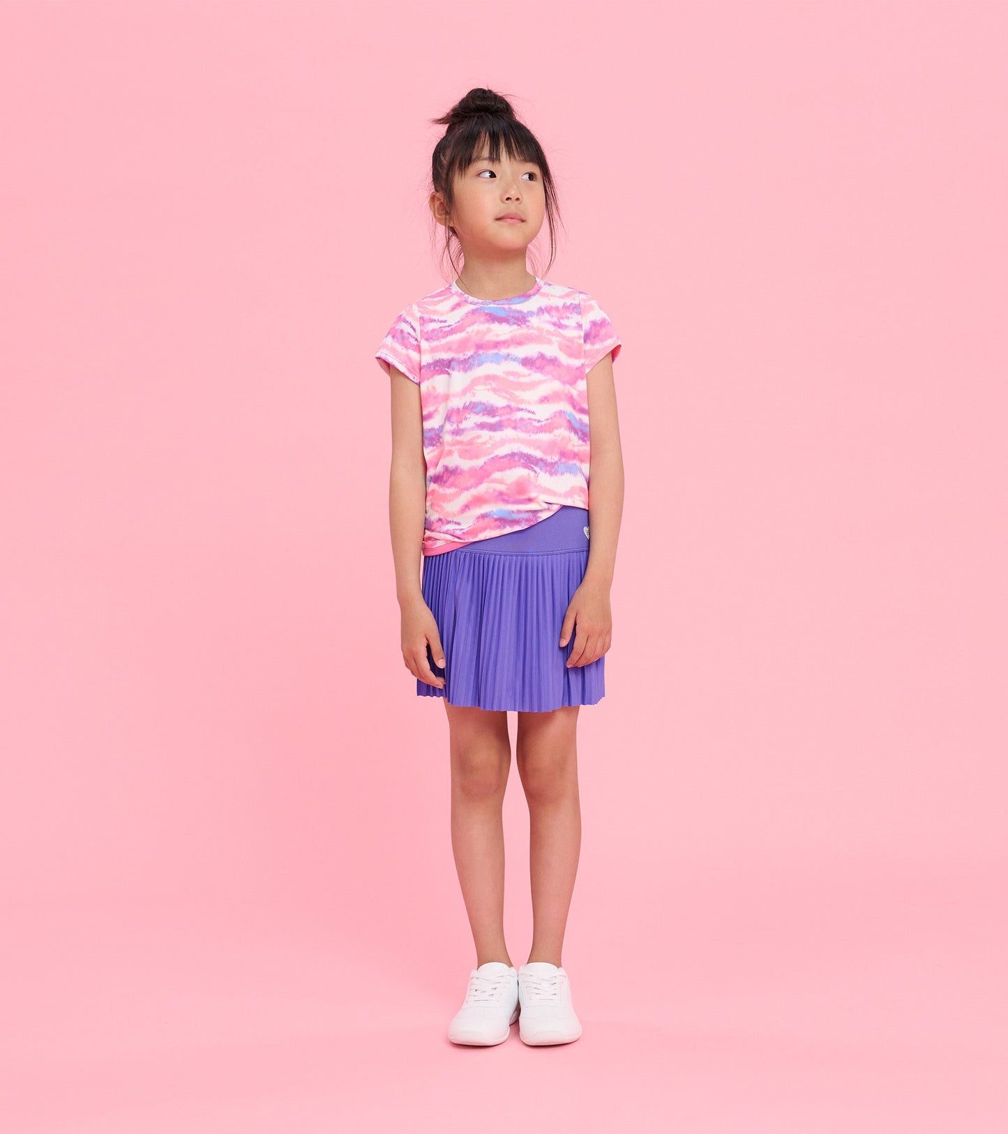 Purple sporty skort with pleated design, paired with a colorful top, worn by a girl standing against a pink background.