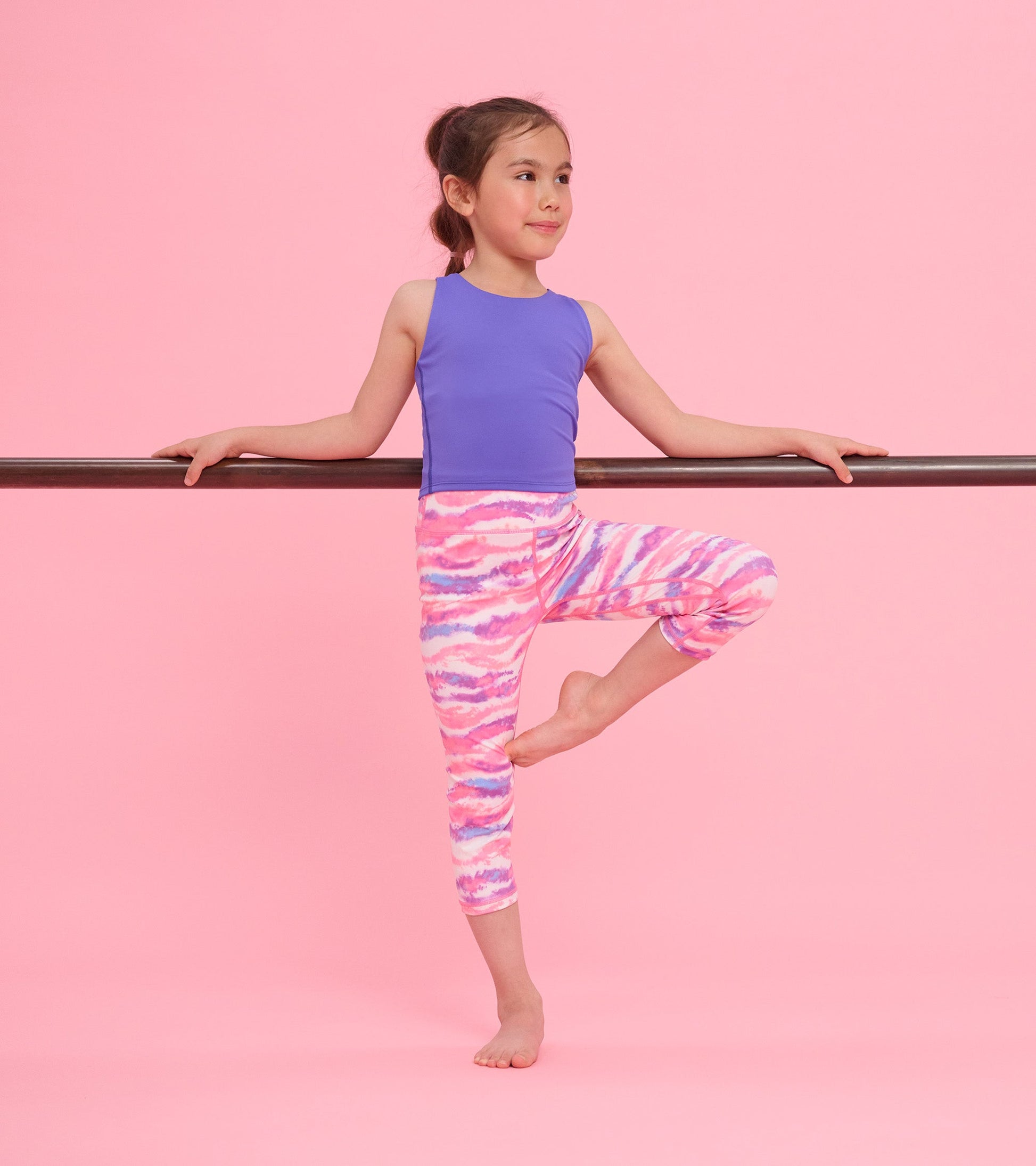 Purple tank top on a girl, paired with colorful tie-dye leggings, posed against a pink background.