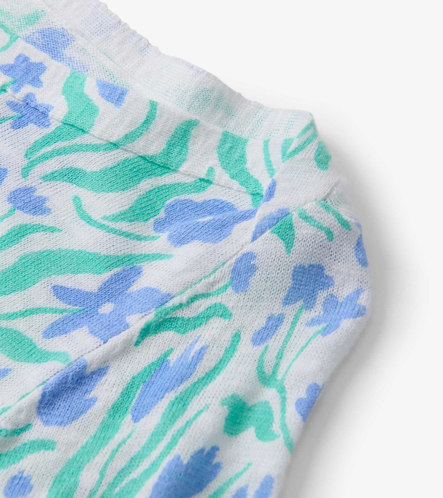 Close-up of a lightweight knit fabric featuring a painted floral pattern in blue and green on a white background.