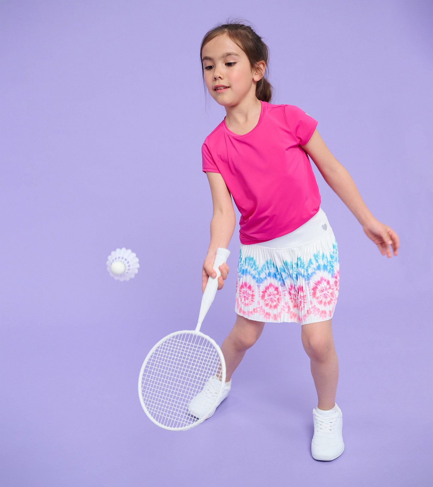 Pink short-sleeve mesh trim t-shirt worn by a girl playing badminton, paired with a colorful tie-dye skirt.