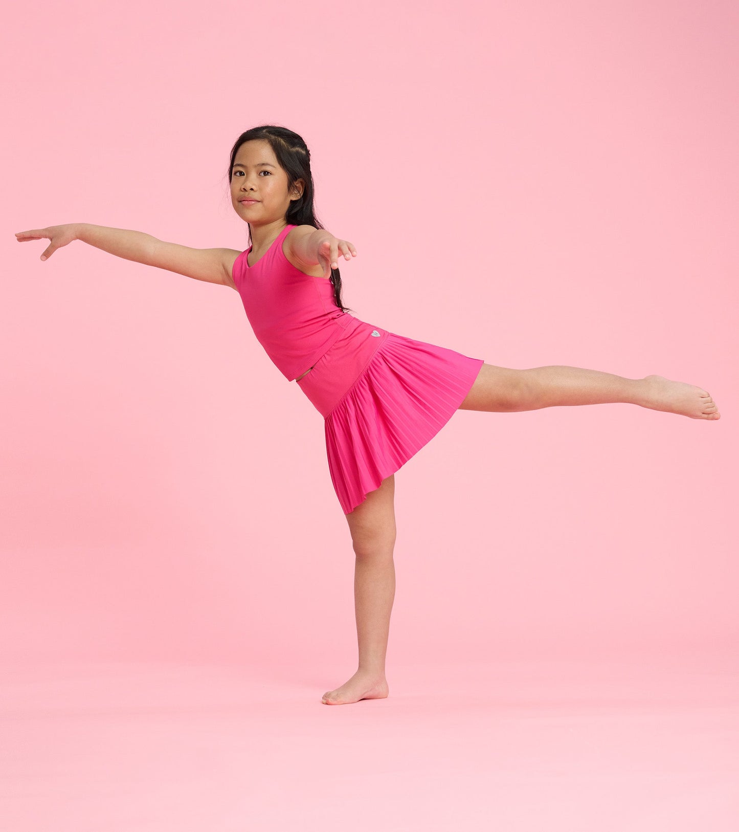 Bright pink sporty skort with pleated design, worn by a girl in a playful pose against a pink background.