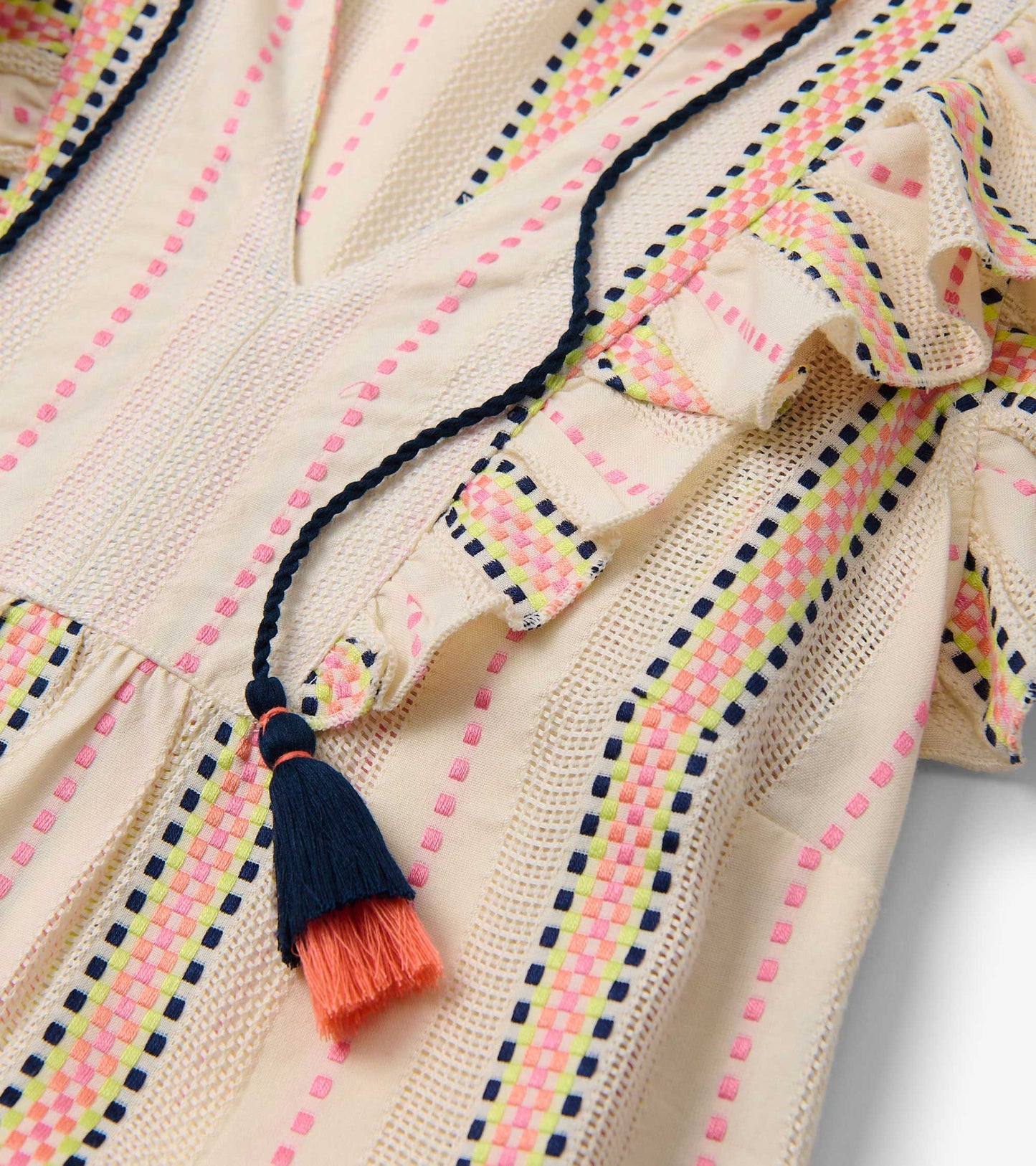 Light cream fabric with colorful ribbon weave stripes and a tassel detail, featuring ruffled edges and a v-neckline.