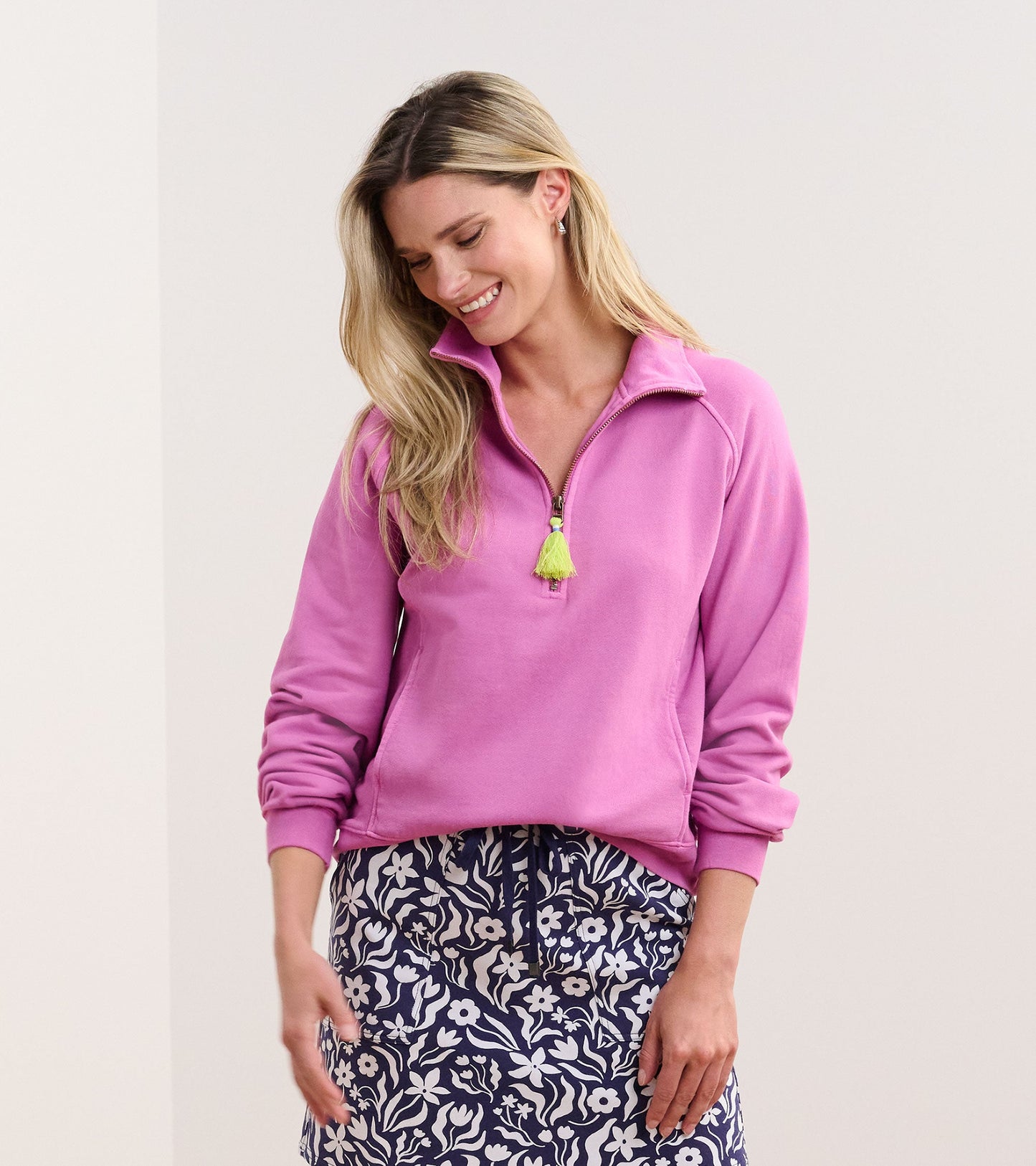 Mock neck pullover in orchid pink with a zip front and a tassel detail, paired with a floral patterned skirt.