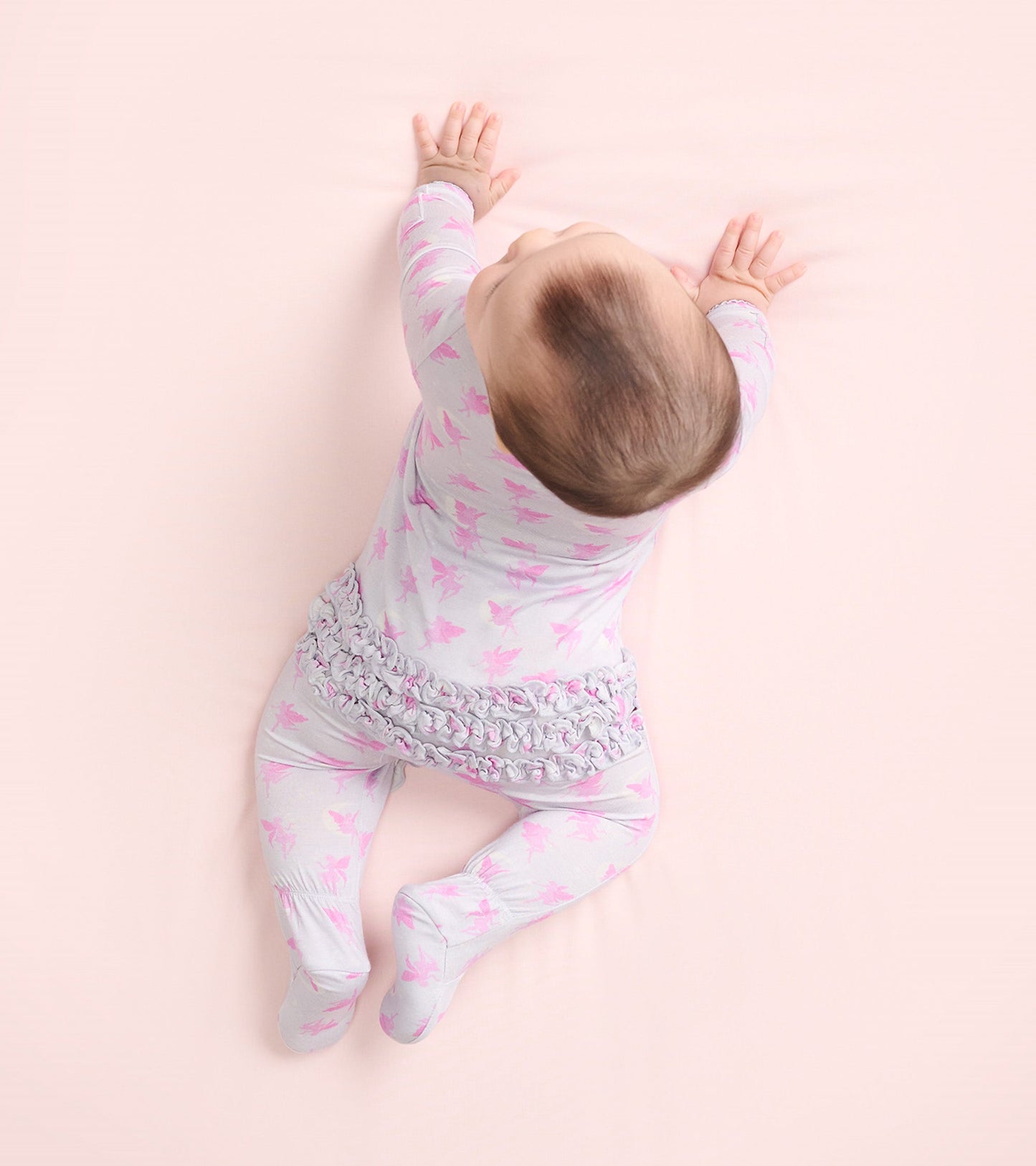Light gray footed sleeper with pink fairy print and ruffled waist, designed for baby girls, shown from above.