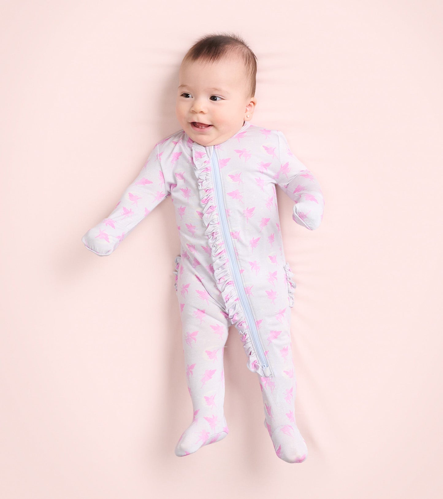 Light gray footed sleeper with pink fairy print and ruffle detail, designed for baby girls, shown on a smiling infant.