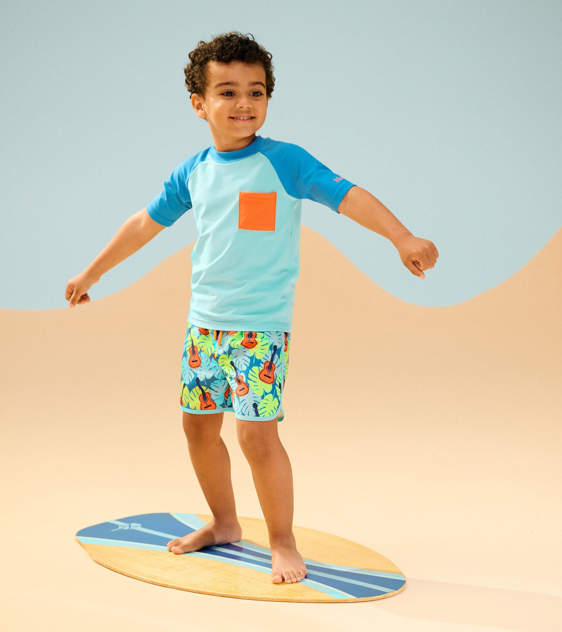 Boys' swim shorts featuring a vibrant tropical guitar pattern, paired with a light blue short-sleeve top.