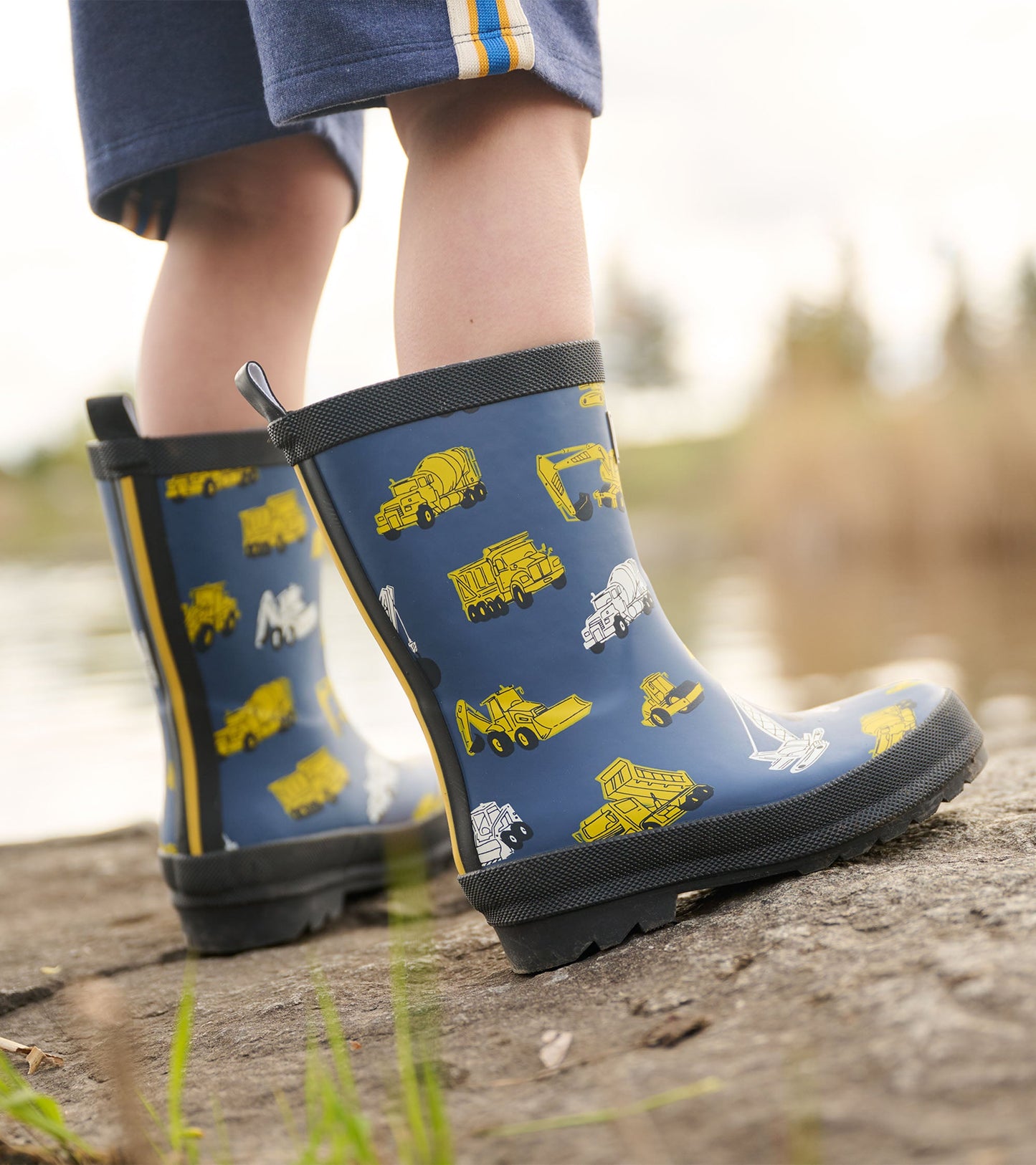 Matte navy rain boots featuring yellow construction vehicle patterns, ideal for outdoor play in wet conditions.