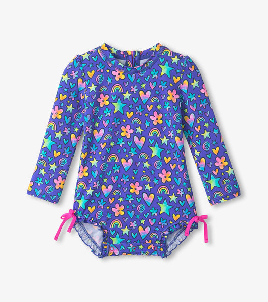 Purple long-sleeve rashguard swimsuit featuring colorful watercolour doodles of stars, hearts, flowers, and rainbows.
