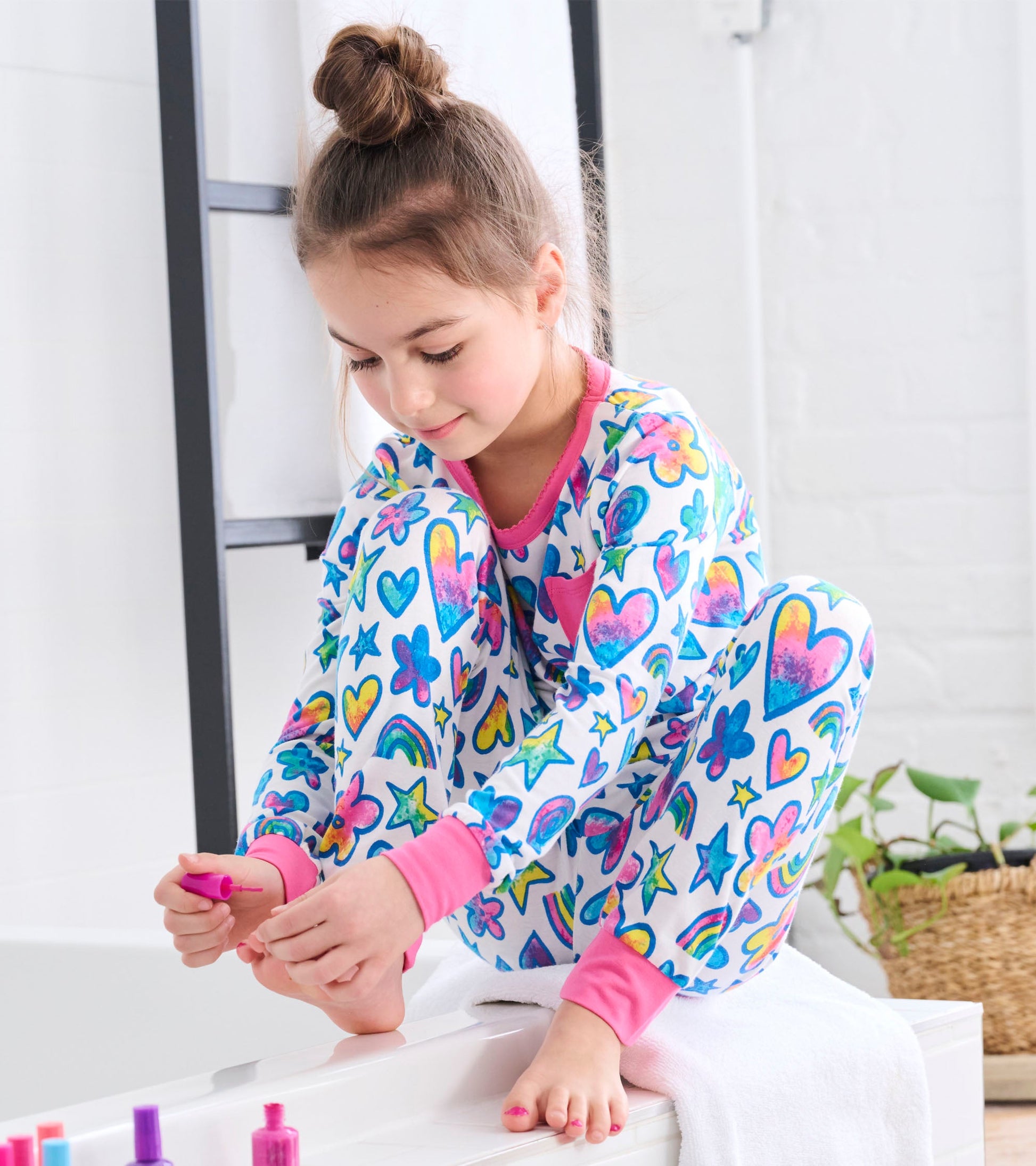 Colorful bamboo pajama set featuring watercolour doodles of hearts, stars, and rainbows, with pink cuffs and neckline.