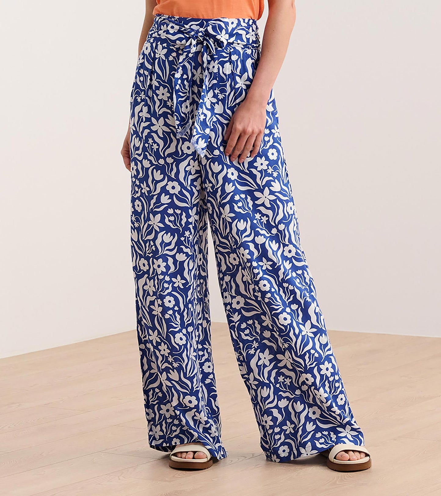 Wide leg pants in blue with a wavy floral pattern, featuring a tie waist and relaxed fit, styled with an orange top.