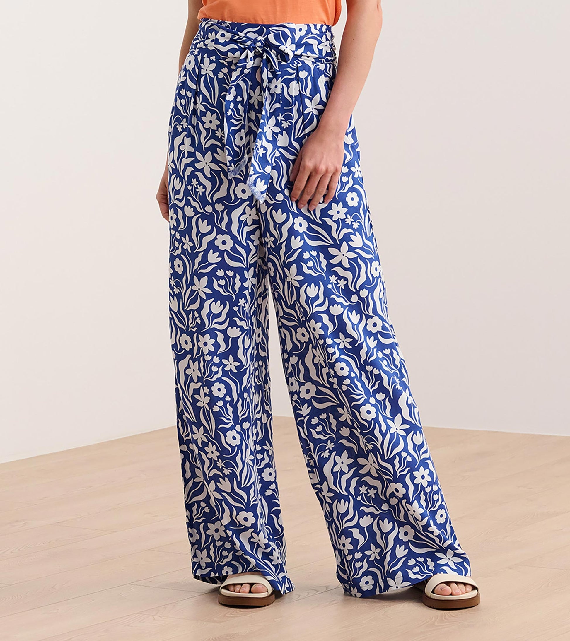 Wide leg pants in blue with a wavy floral pattern, featuring a tie waist and relaxed fit, styled with an orange top.