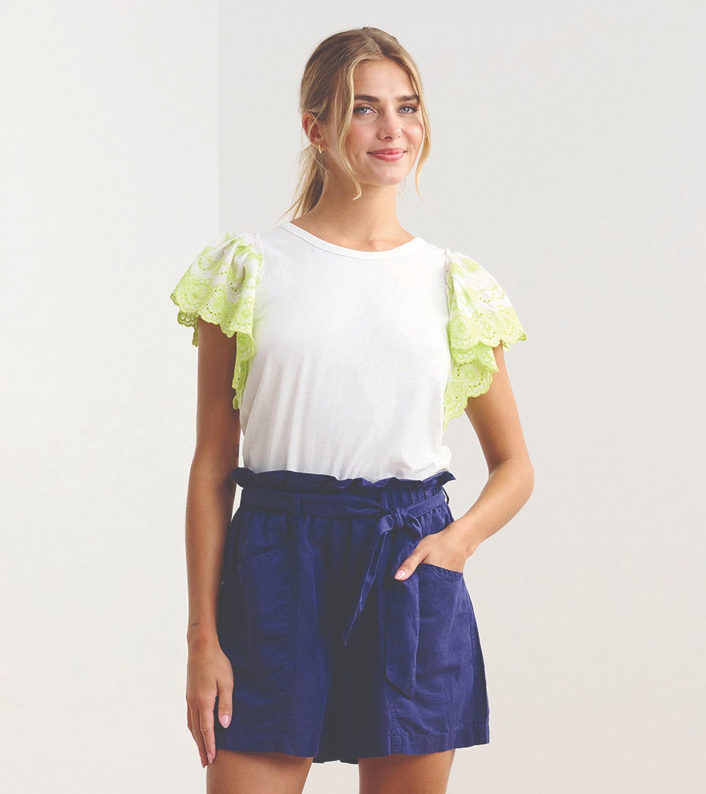 White tank top featuring eyelet sleeves in bright green, paired with navy shorts, styled for a casual look.