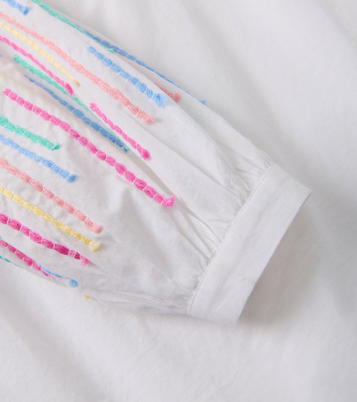 White gauze tunic featuring colorful embroidered stripes on the sleeves.