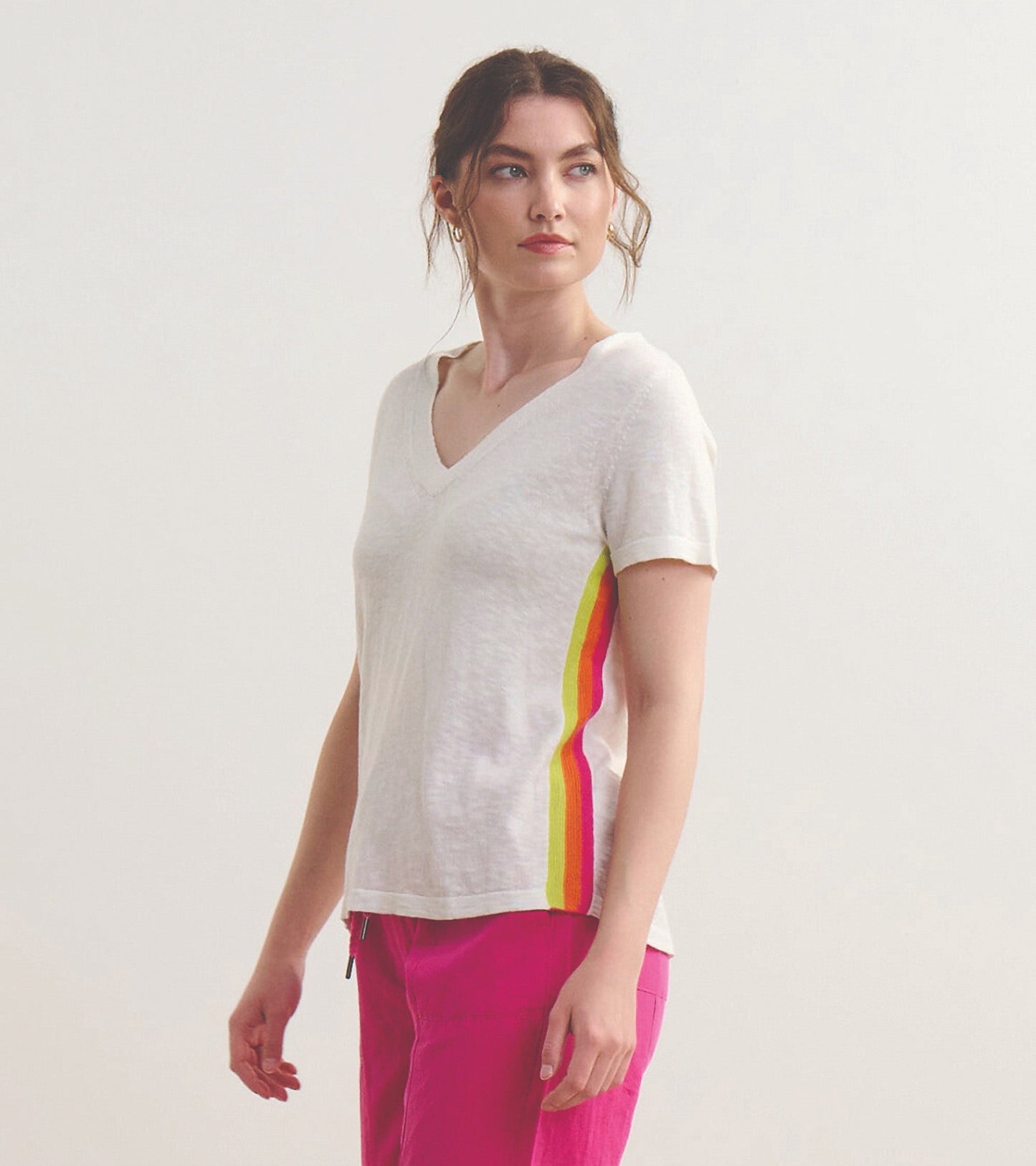White V-neck knit tee featuring colorful stripes on the sides, styled with pink pants.