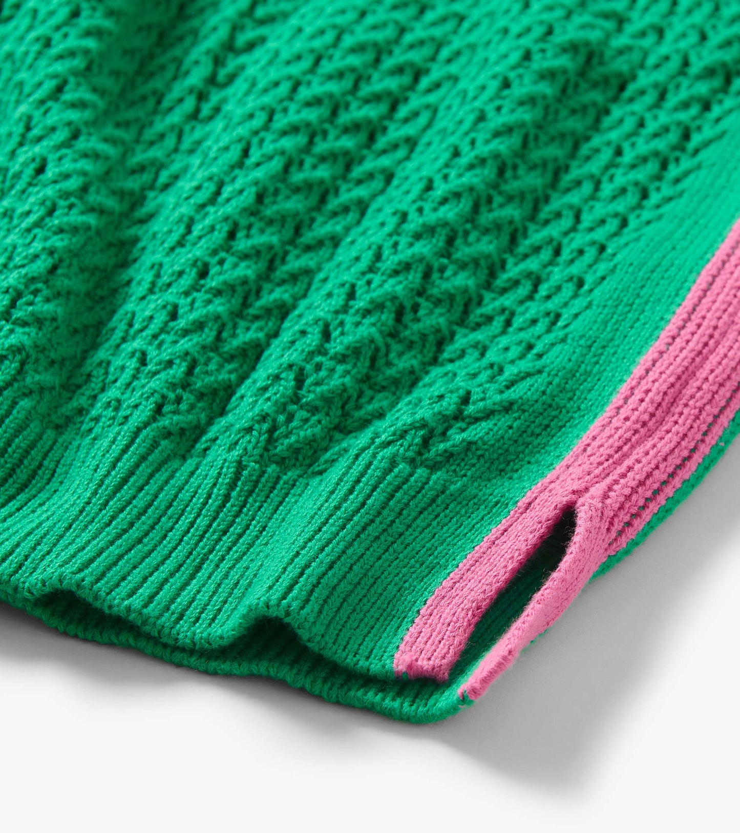 Close-up of a green cable-knit tank top with pink trim and ribbed hem