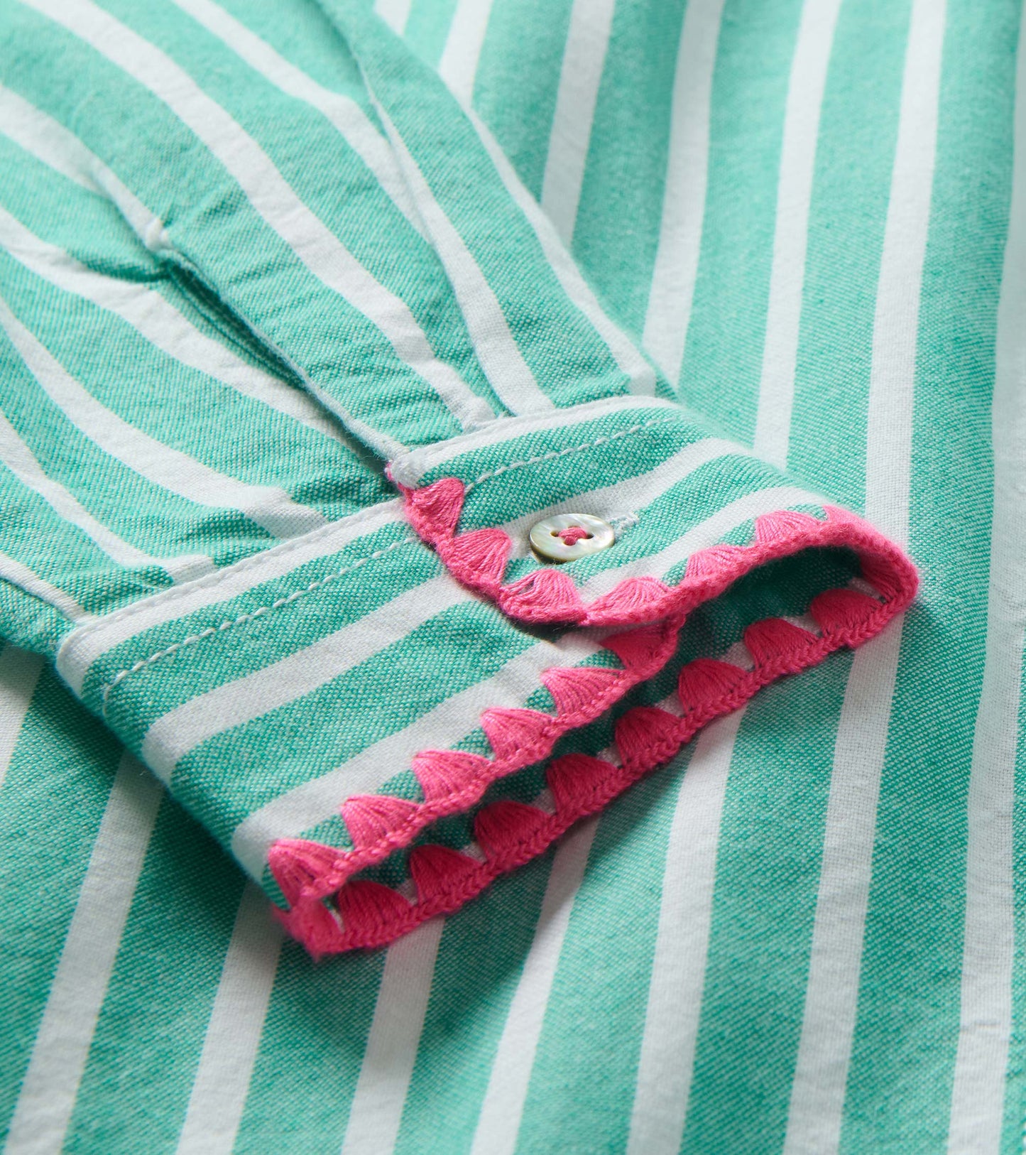 Close-up of a mint green and white striped shirt dress cuff with pink scalloped trim and button detail