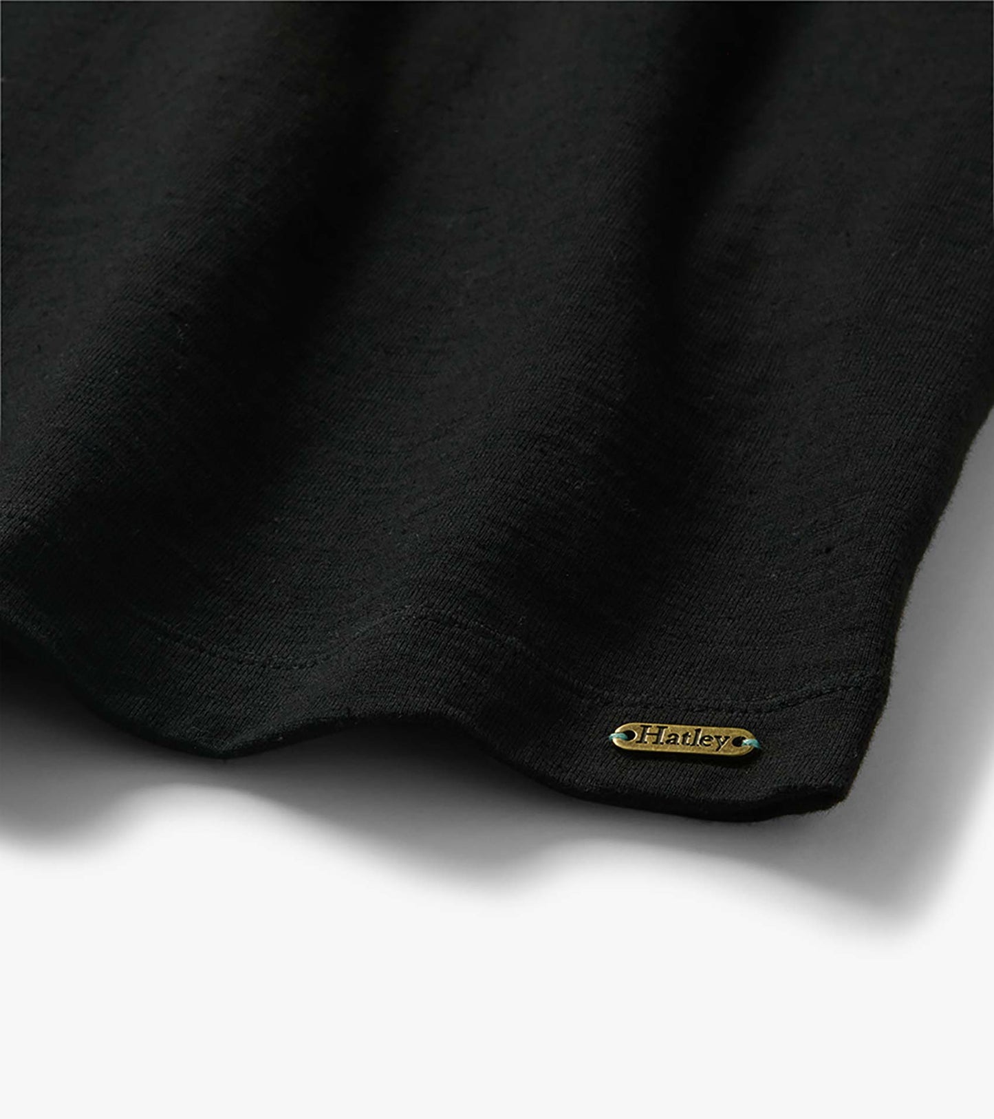 Black tee dress hem close-up with small gold Hatley logo plate near the bottom edge