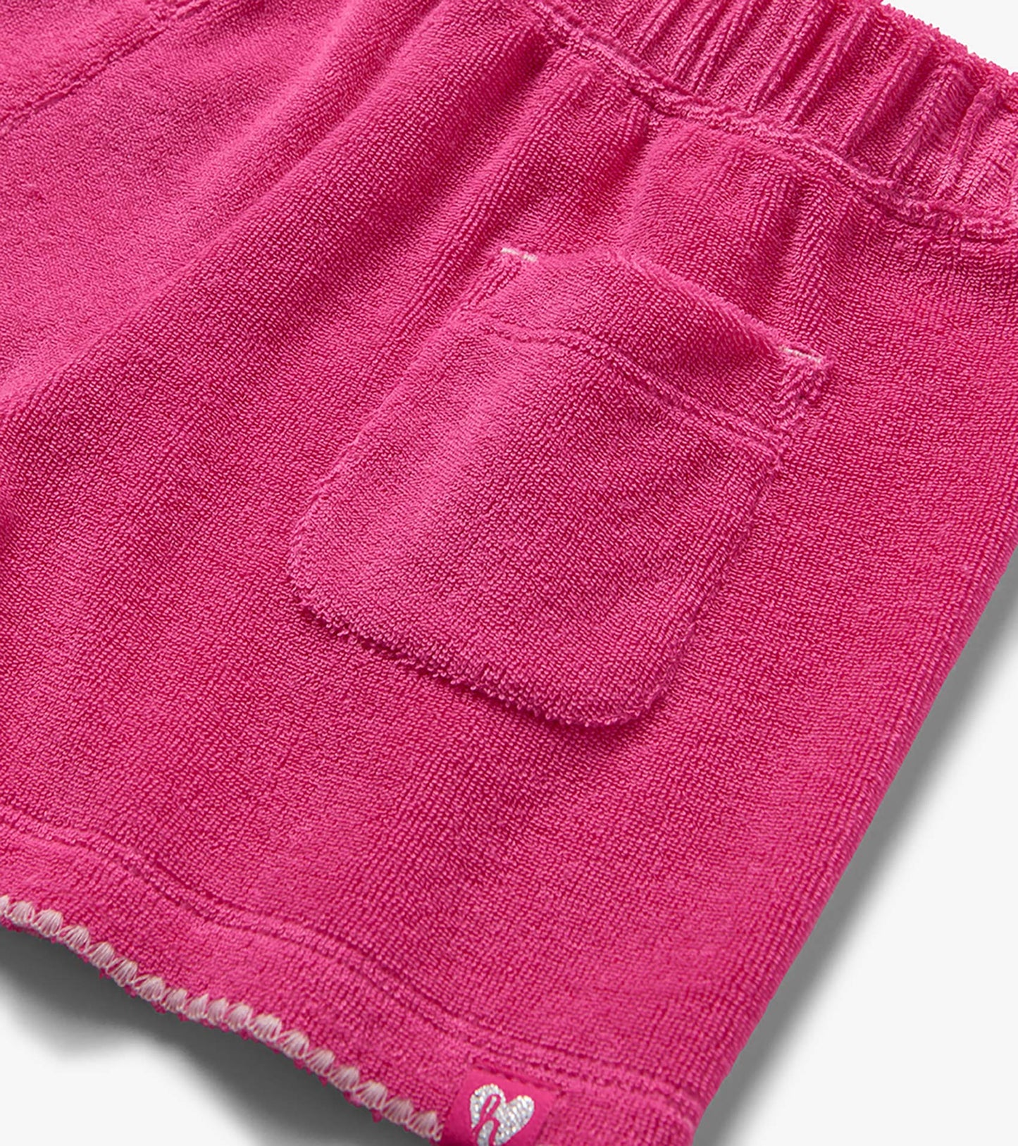 Pink textured knit shorts with elastic waistband, back pocket, and small heart patch, close-up view