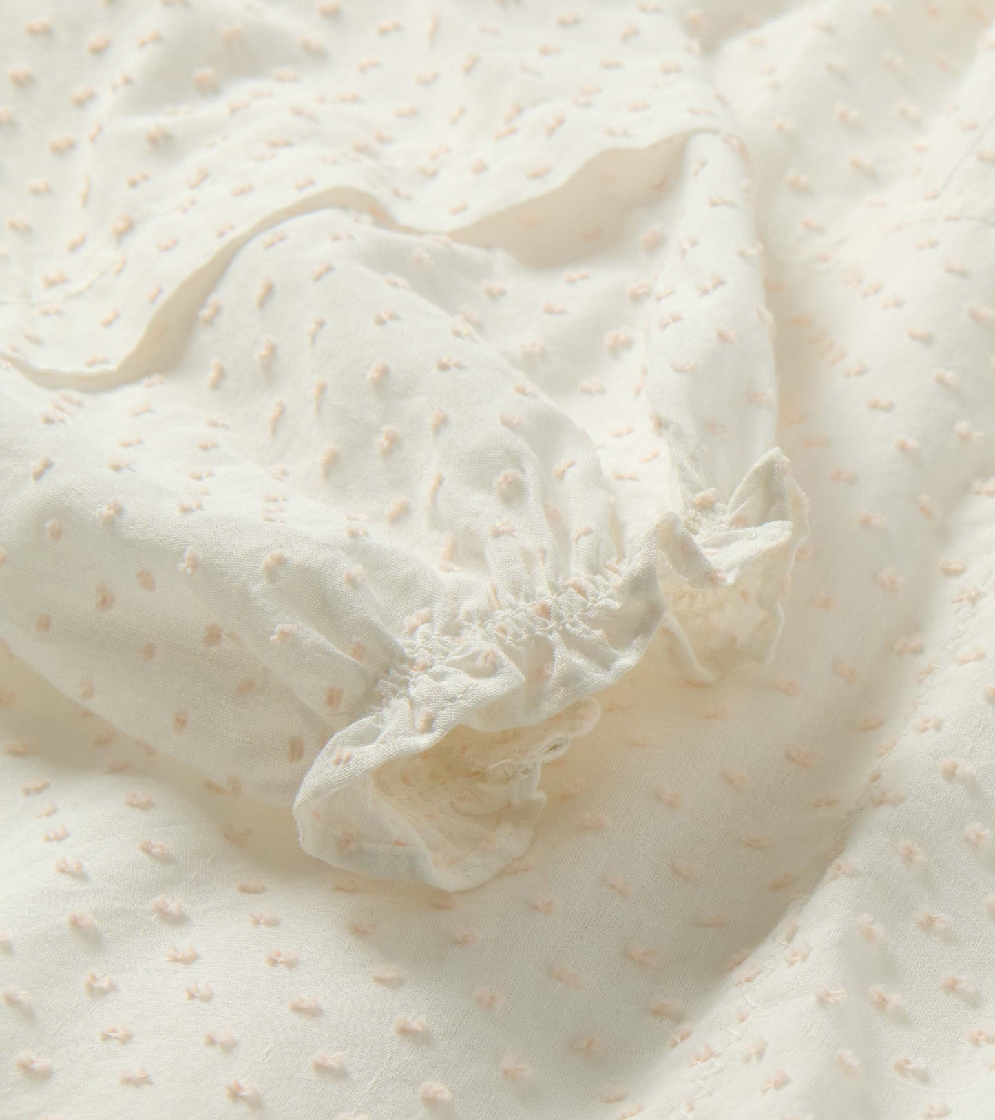Close-up of cream Swiss dot fabric with soft blush textured dots and gathered ruffled hem detail