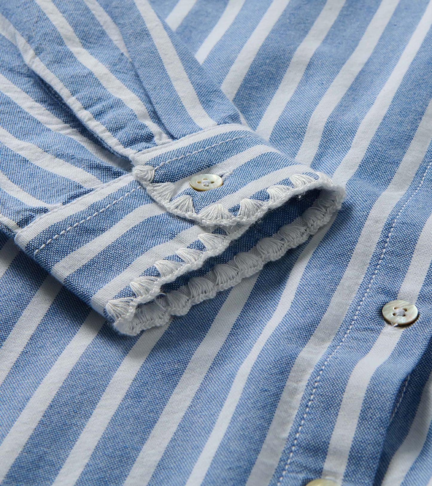 Close-up of blue and white striped sleeve cuff with button tab and white embroidered trim