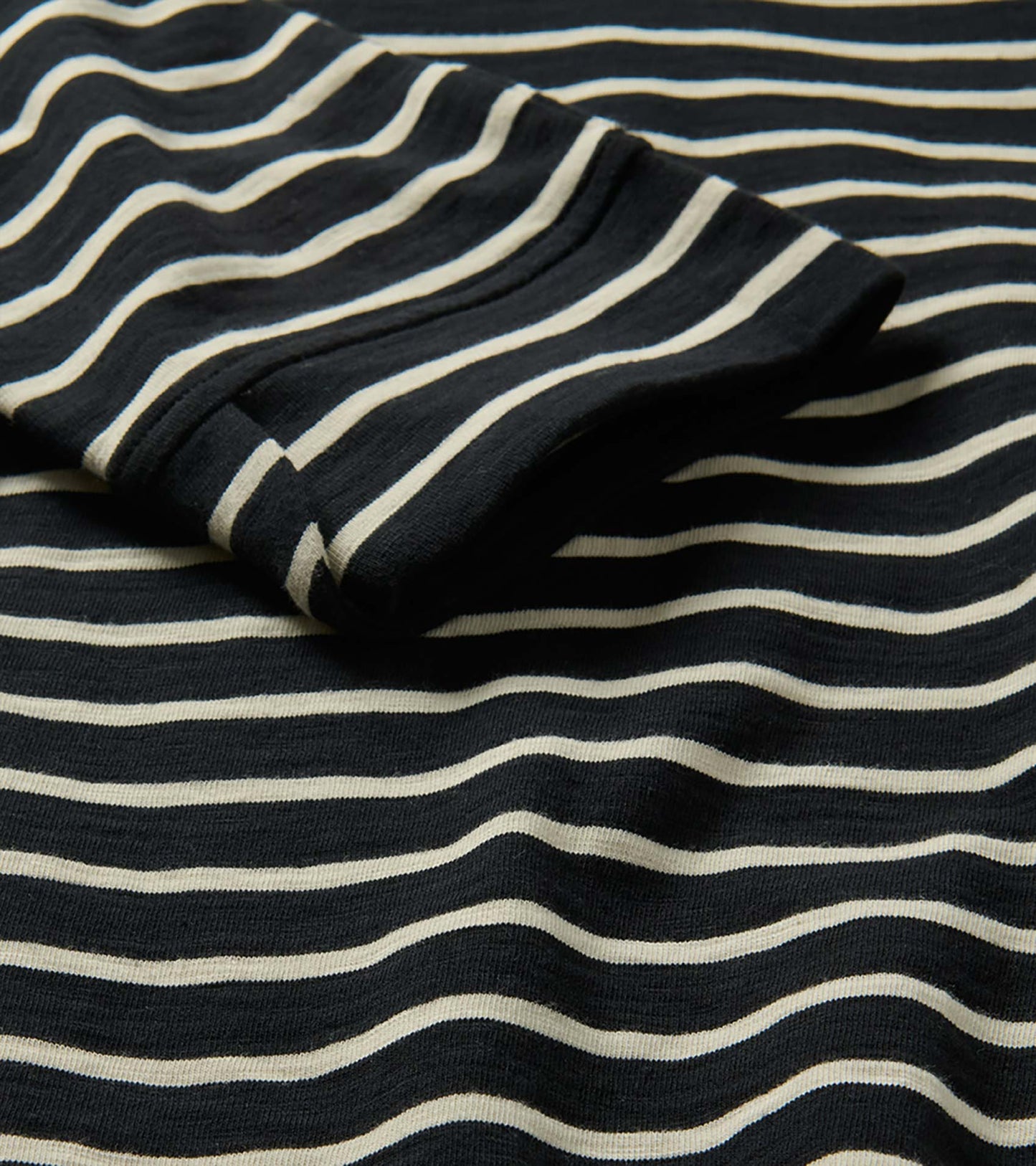 Close-up of black fabric with ivory horizontal stripes and a folded sleeve detail