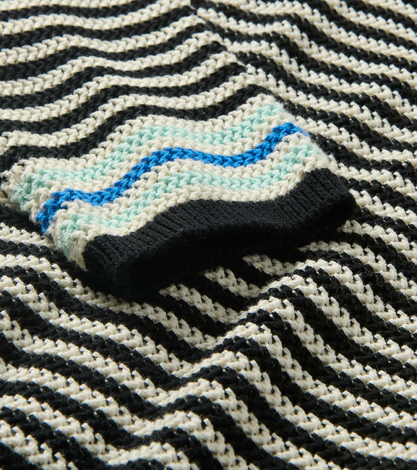 Close-up of sweater cuff with black trim, aqua and blue stripes, and black and white pointelle knit