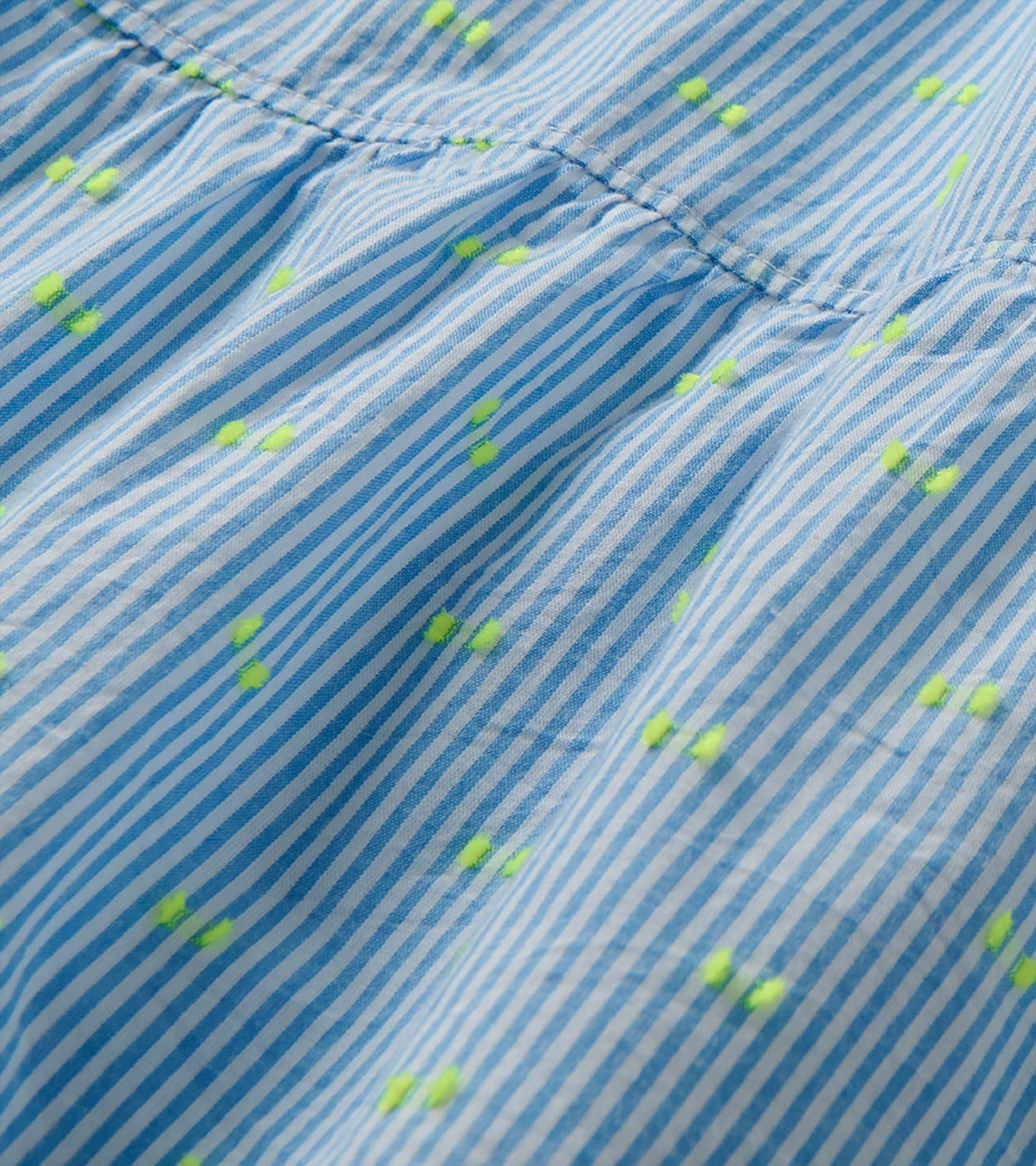 Close-up of blue and white striped dress fabric with neon yellow dots and a gathered seam detail