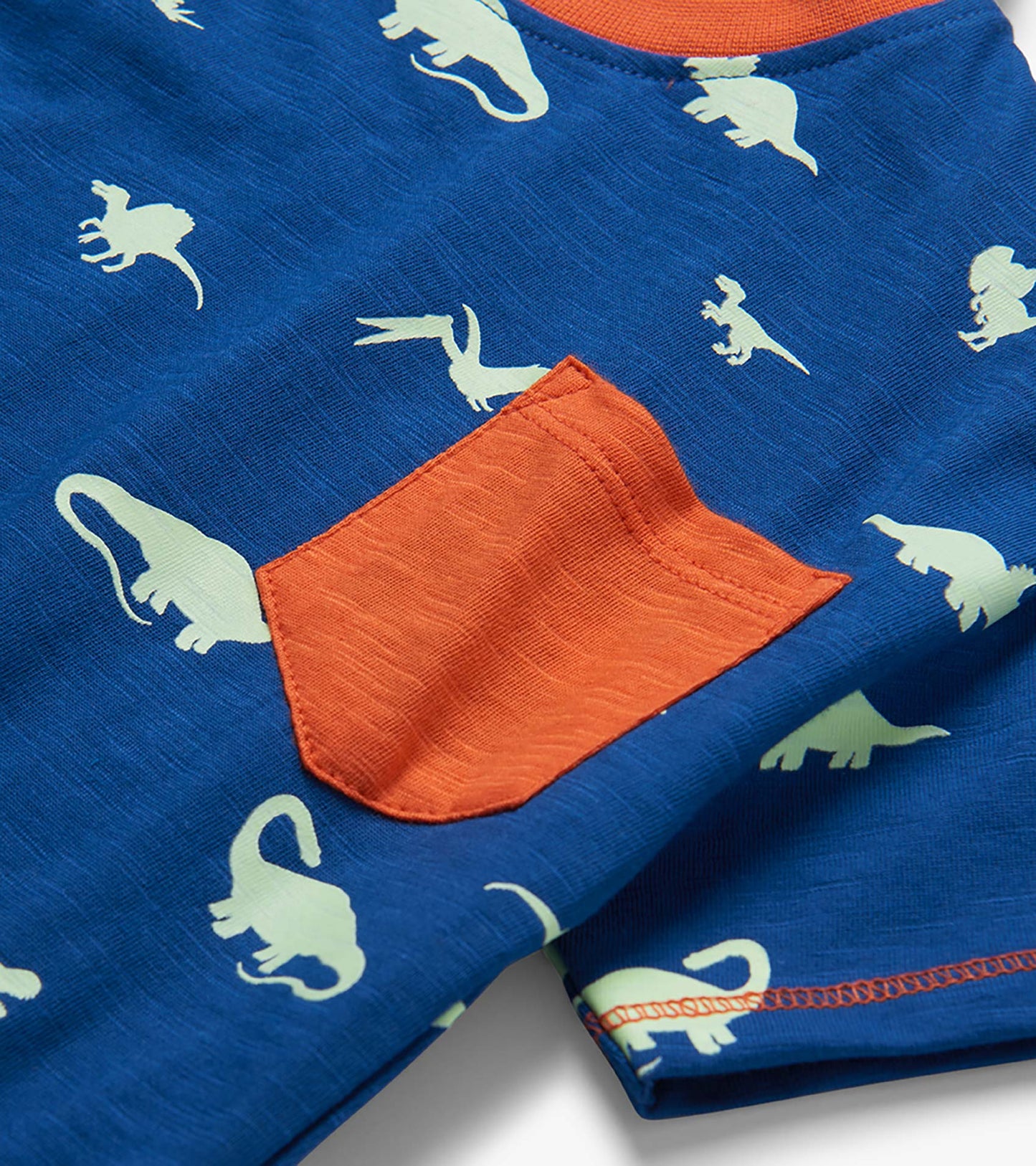 Blue toddler T-shirt with white dinosaur print and orange chest pocket, close-up front view