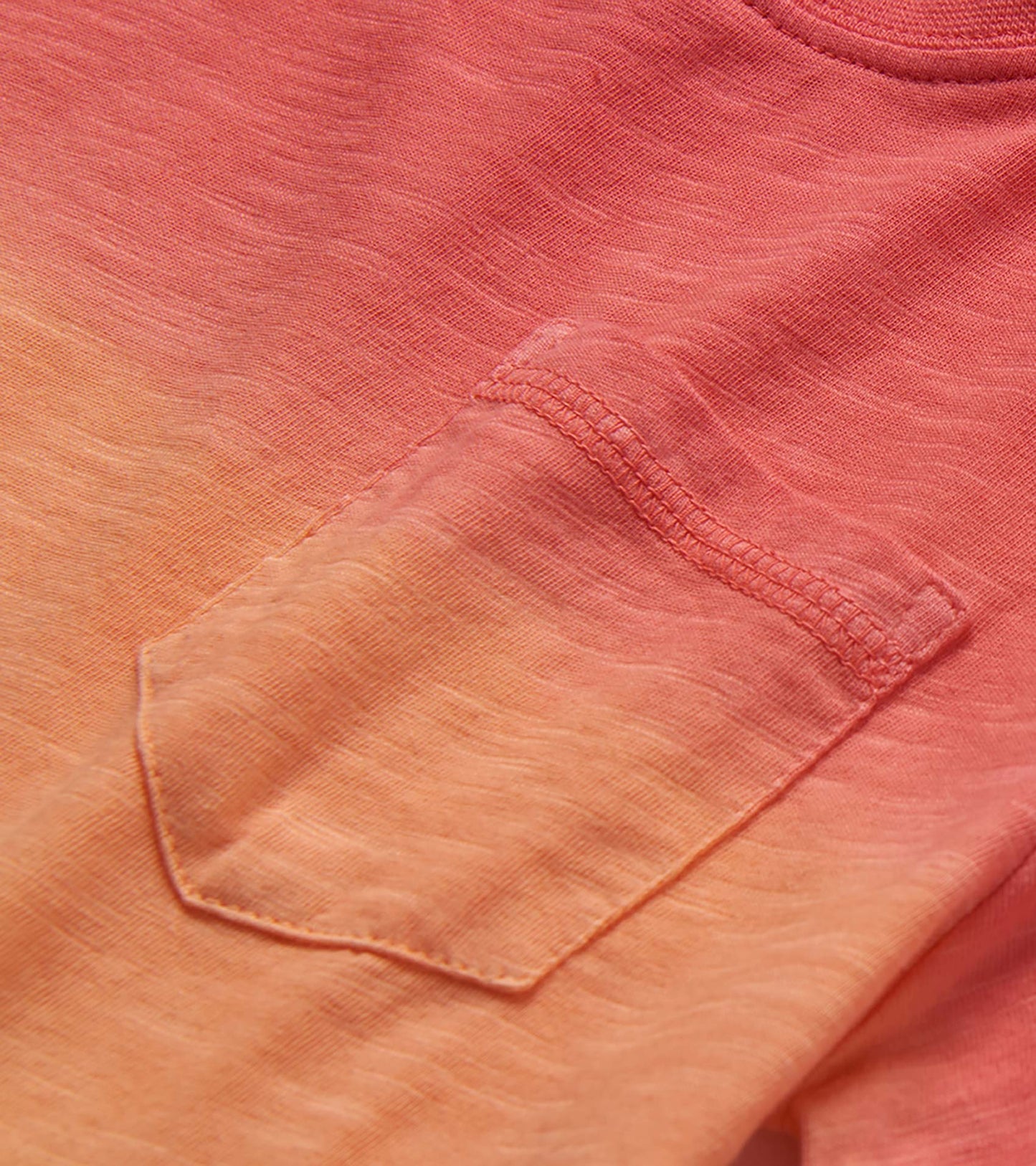 Close-up of a coral and peach gradient knit T-shirt pocket with stitched detail