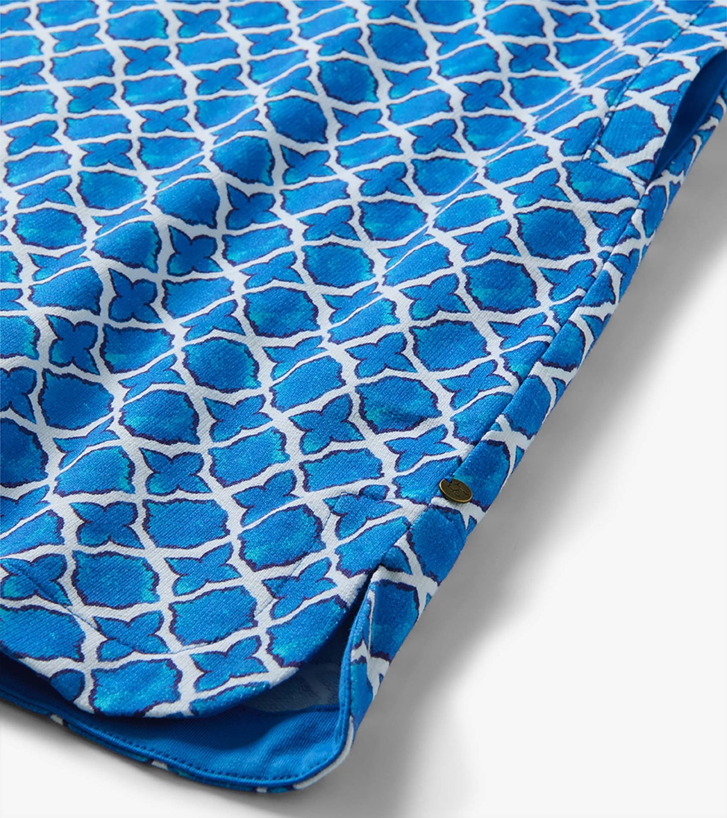 Blue and white medallion print dress fabric with curved hem and button detail, close-up view