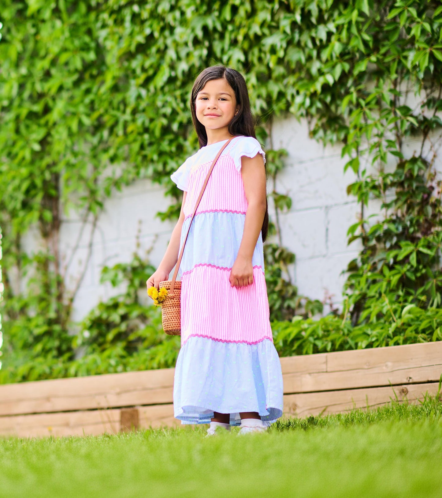 Side view of girl wearing a pink and blue tiered striped midi dress with scalloped trim