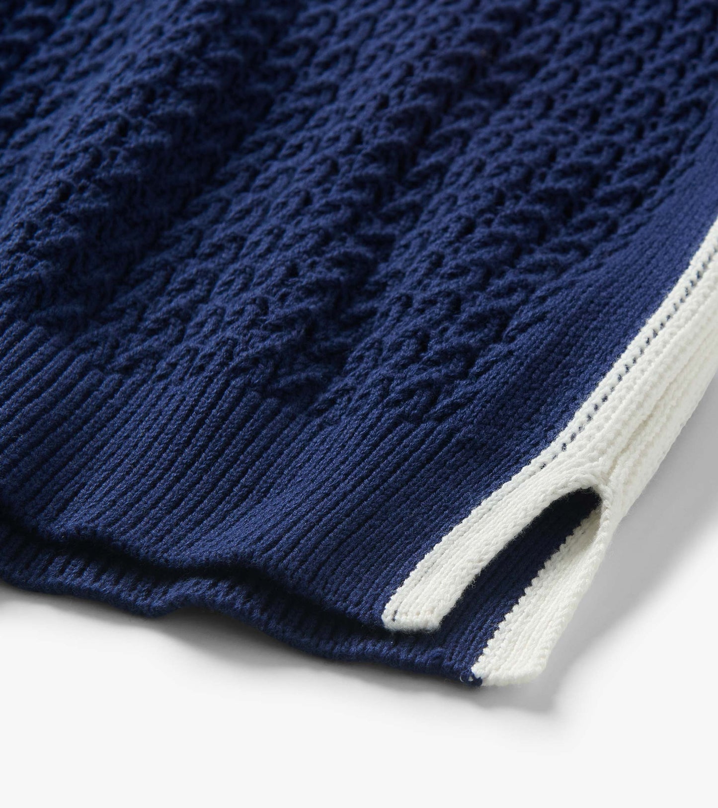Close-up of a navy knit tank with textured cable pattern and white trim at the hem and side slit
