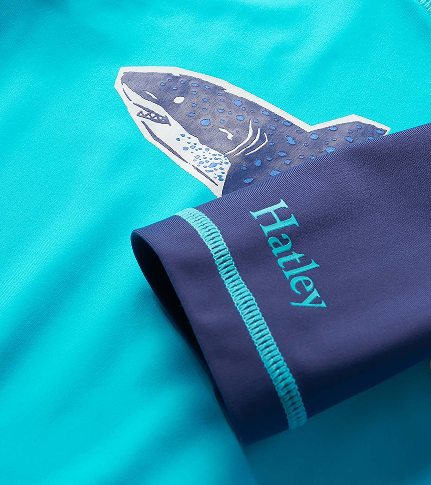 Turquoise boys rashguard with navy sleeve, shark graphic, and flatlock seam detail