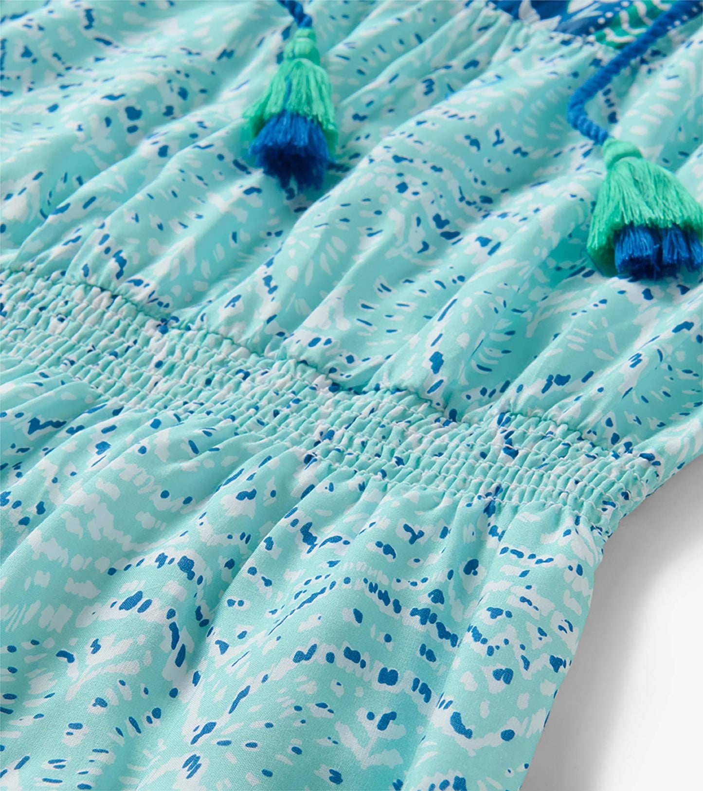 Close-up of the Chloe Dress in beach glass ikat with a smocked waist and blue-green tassel ties