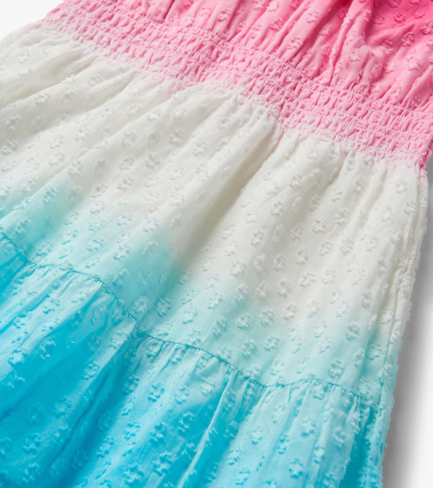 Close-up of a pink-to-white-to-blue dip-dye gathered dress with textured fabric and ruffled tiers