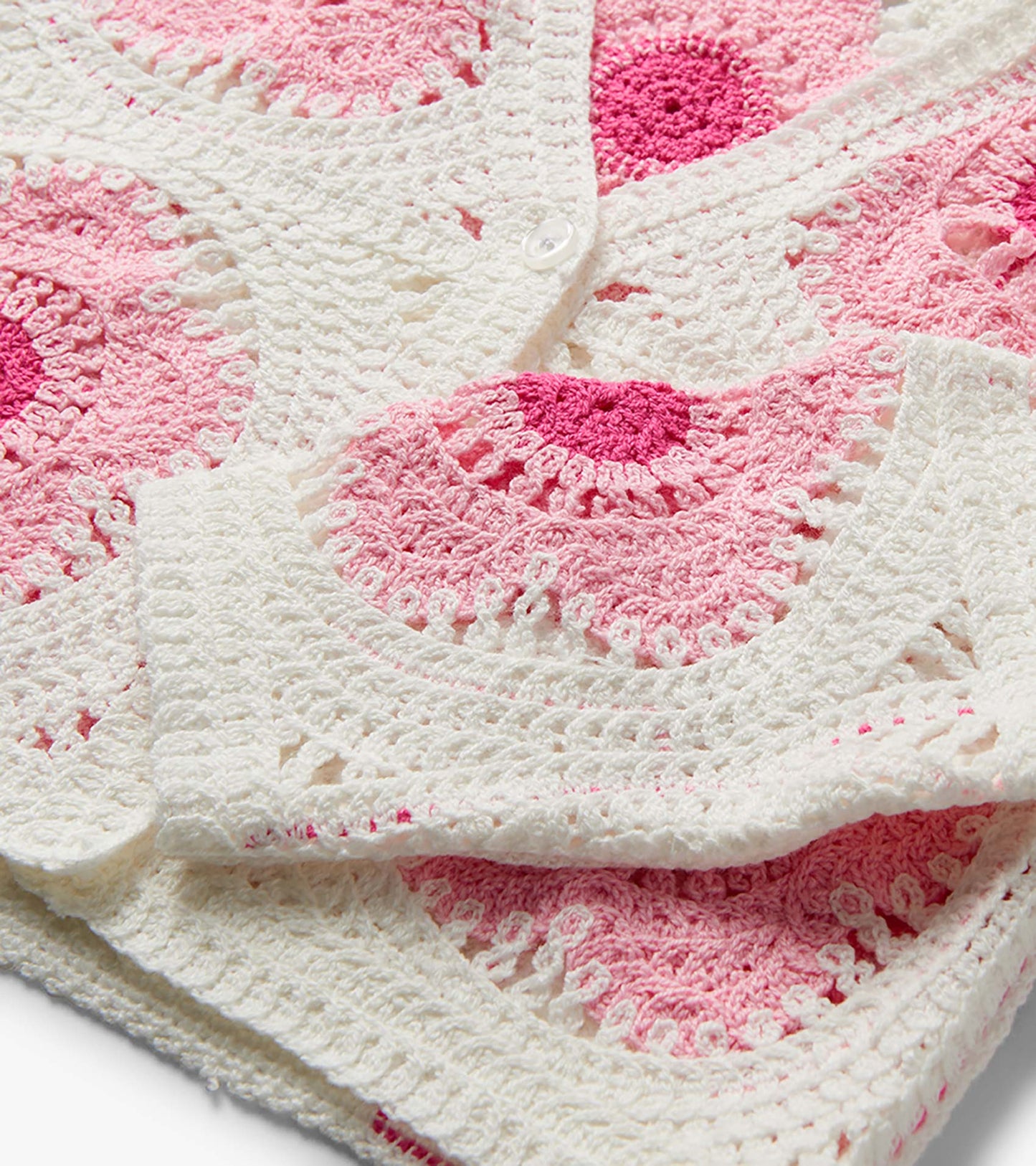 Pink and cream crochet cardigan with floral pattern and white button closure, folded close-up