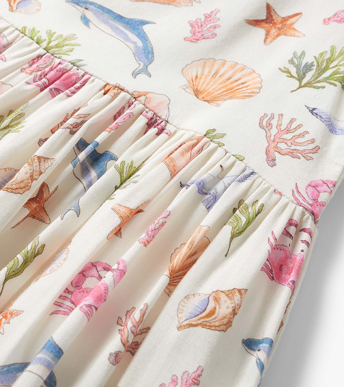 Cream girls dress with colorful seashell, coral, and dolphin print and gathered smocked waist detail