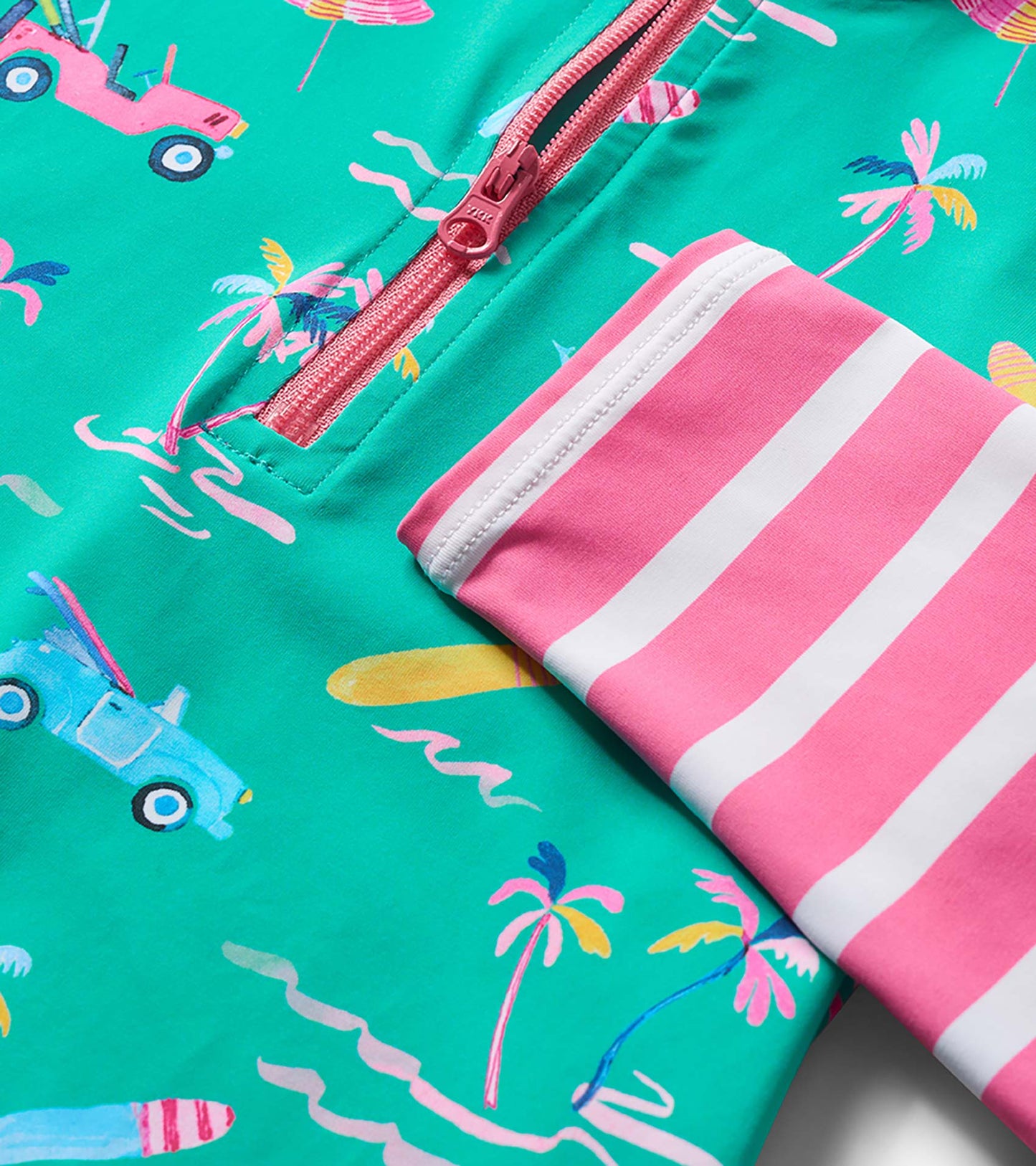 Close-up of a teal girls' rashguard with tropical car and palm print, pink zipper, and pink striped sleeve cuff