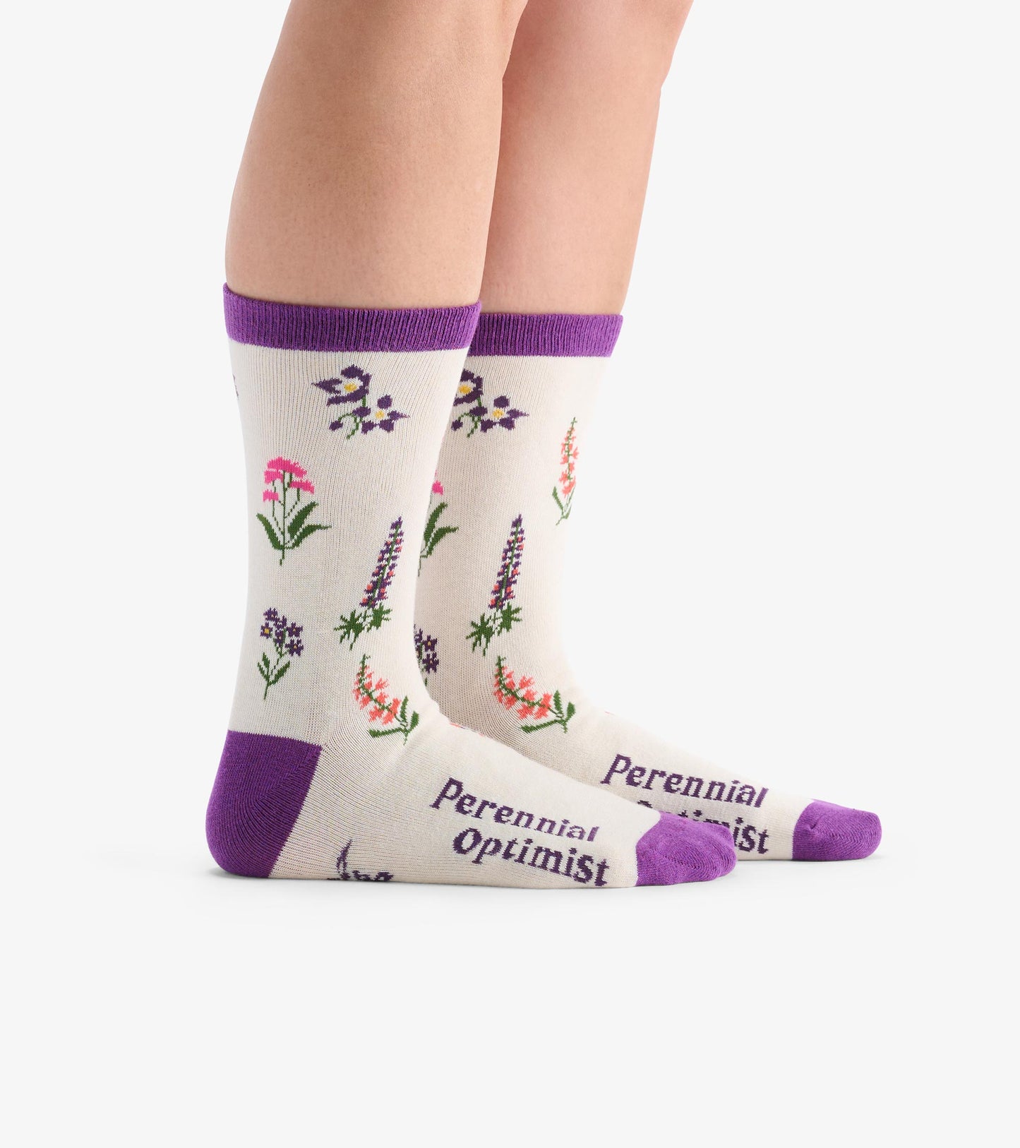 Cream crew socks featuring colorful wildflower patterns and purple accents, with "Perennial Optimist" text on the foot.