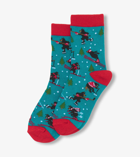 Turquoise crew socks with red cuffs featuring skiing bears and pine trees in a winter scene.
