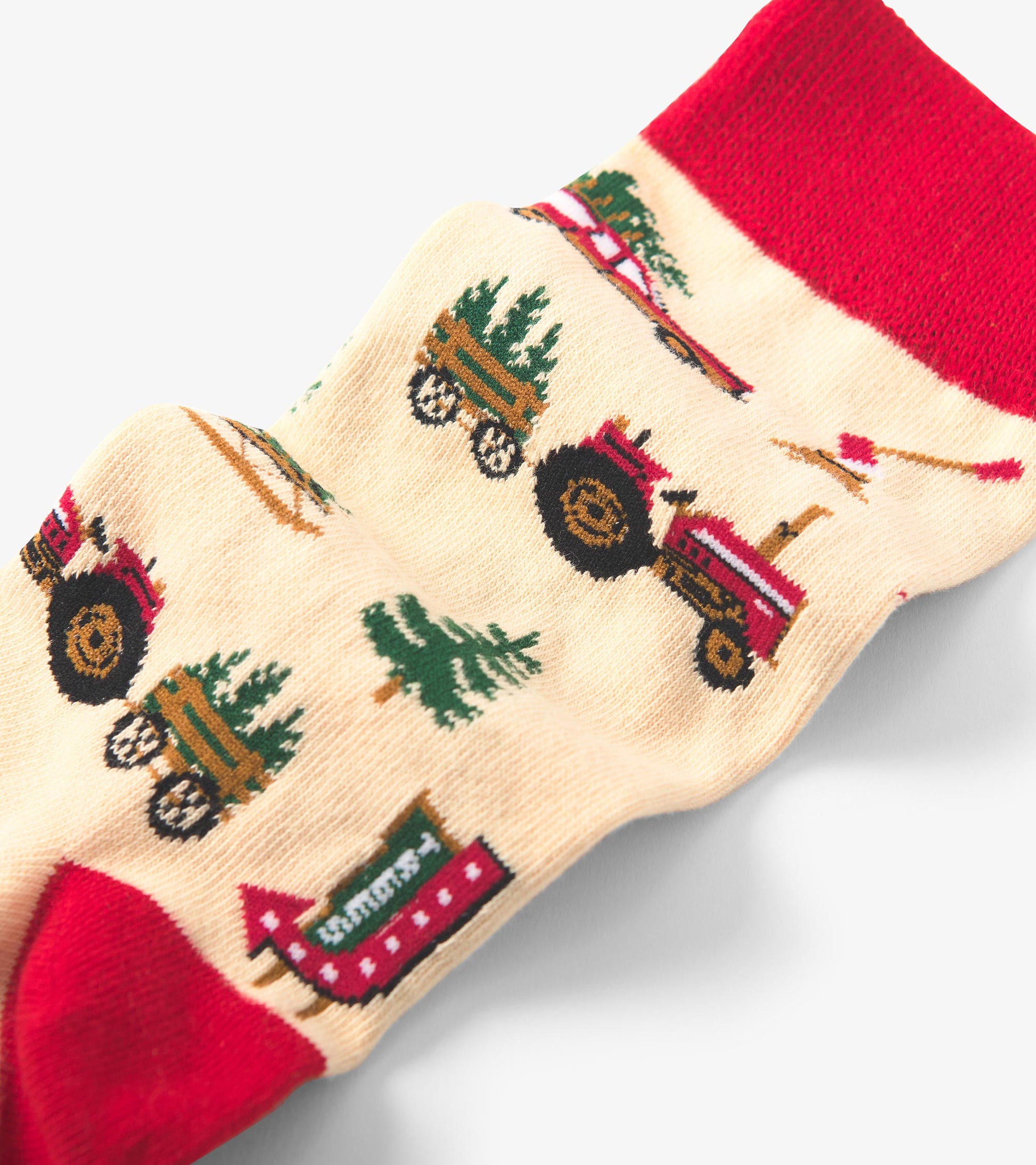 Beige crew socks featuring red accents and festive patterns of tractors and Christmas trees. One size fits all.