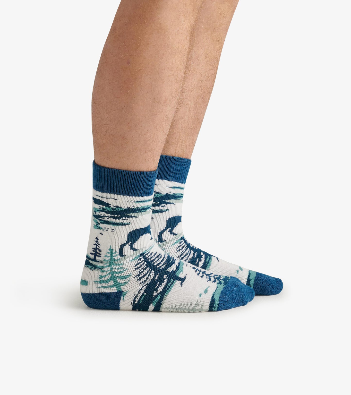 Cozy socks featuring a moose and forest design in blue, green, and white, shown on a person's feet.