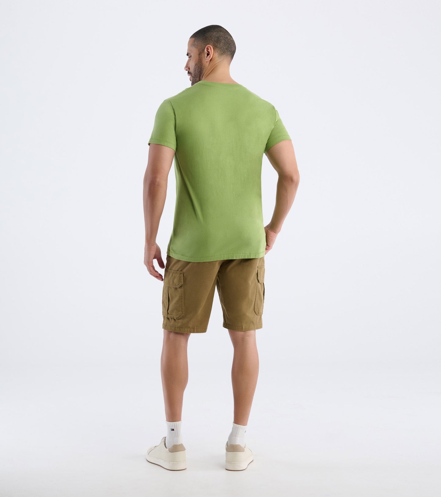 Green short-sleeve men's tee, viewed from the back, paired with khaki cargo shorts and white sneakers.