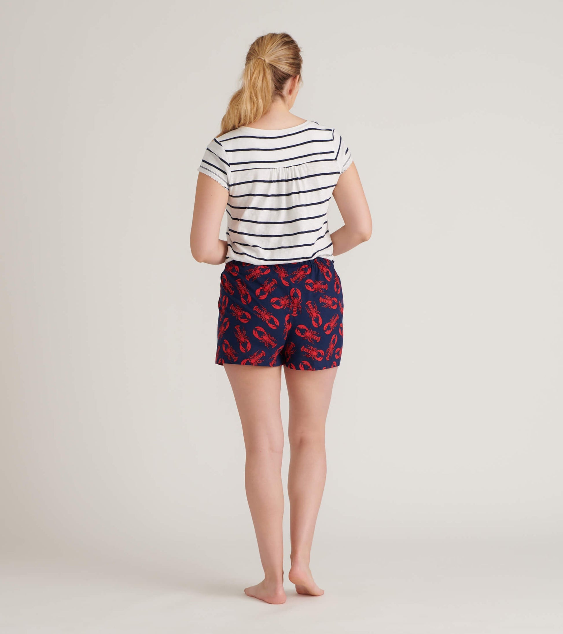 Women's striped V-neck tee in white and navy, paired with lobster-print shorts, viewed from the back.
