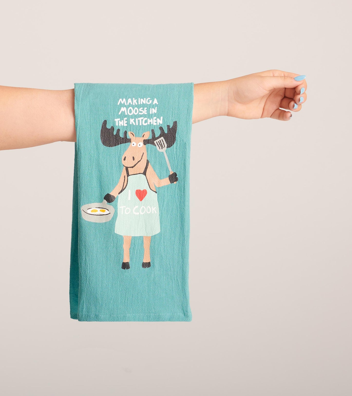 Turquoise tea towel featuring a cartoon moose in an apron holding a spatula and bowl, with the text "Making a Moose In The K…