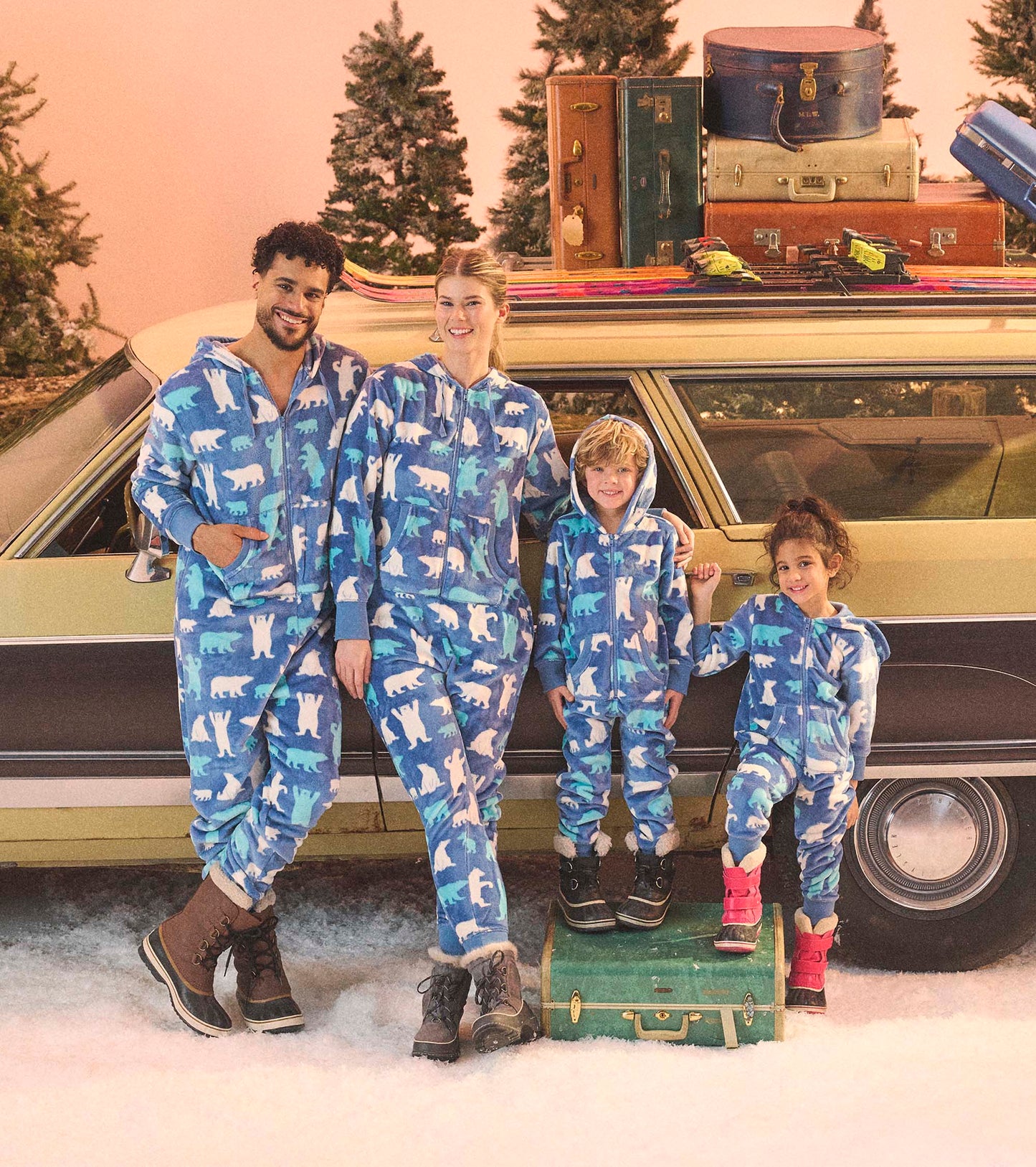 Blue fleece jumpsuits with polar bear patterns, worn by adults and children, set against a snowy backdrop.