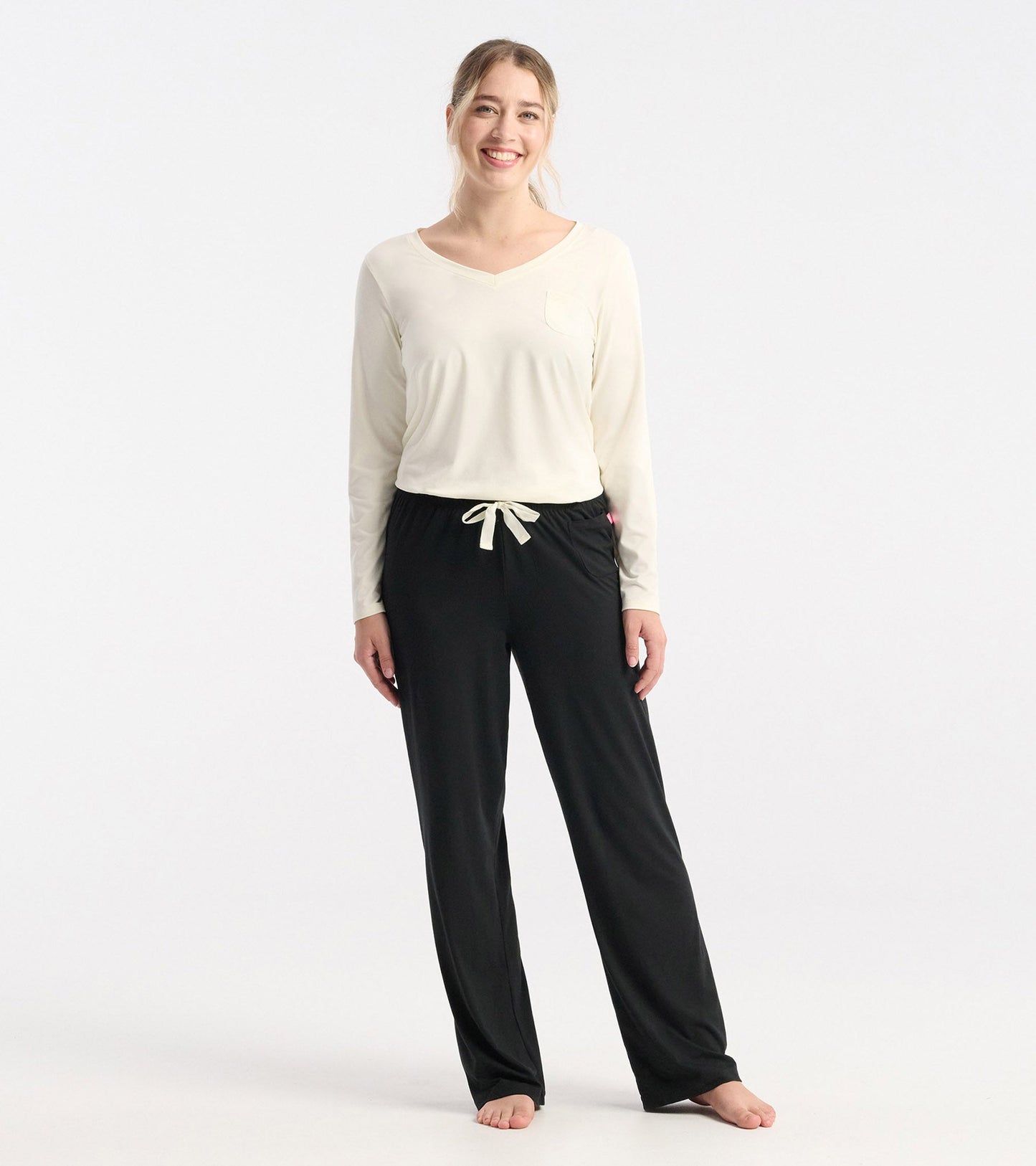 Cream long sleeve t-shirt with a v-neck and pocket, paired with black drawstring pants, worn by a smiling model.