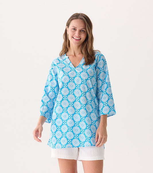 Blue tunic featuring a gradient floral pattern, V-neckline, and three-quarter sleeves, styled with white shorts.