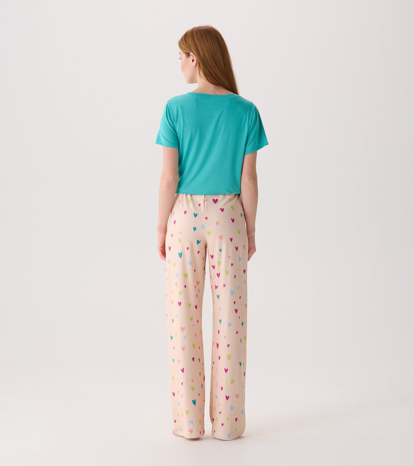 Back view of women's pajama pants in light pink with colorful heart patterns, paired with a teal short-sleeve top.